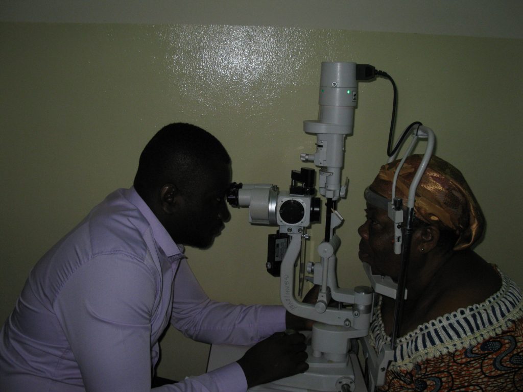 A Ghanaian optometrist examines an older woman's eyes with a slit lamp