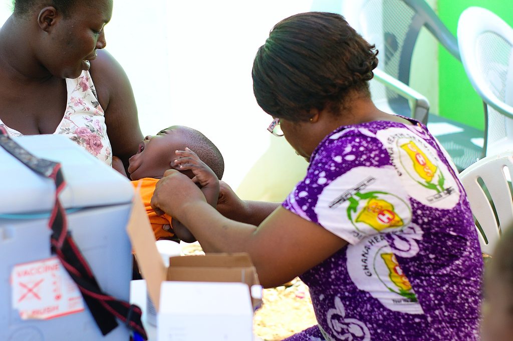 A Ghana Health Service nurse vaccinates a baby held by its mother