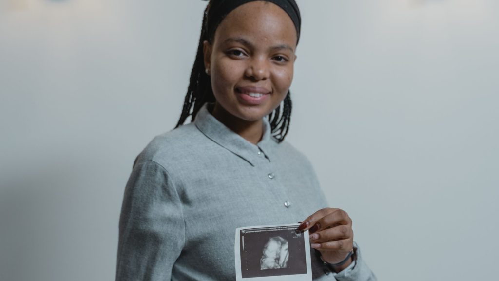 A smiling pregnant woman holds a strip of ultrasound scan images